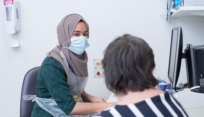 patient consulting with masked pharmacist at a desk with a computer in the background